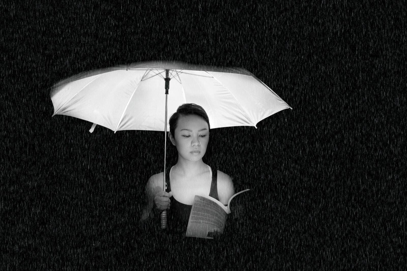 A woman reads calmly beneath a white umbrella in heavy rain — a study in being prepared before the weather turns.